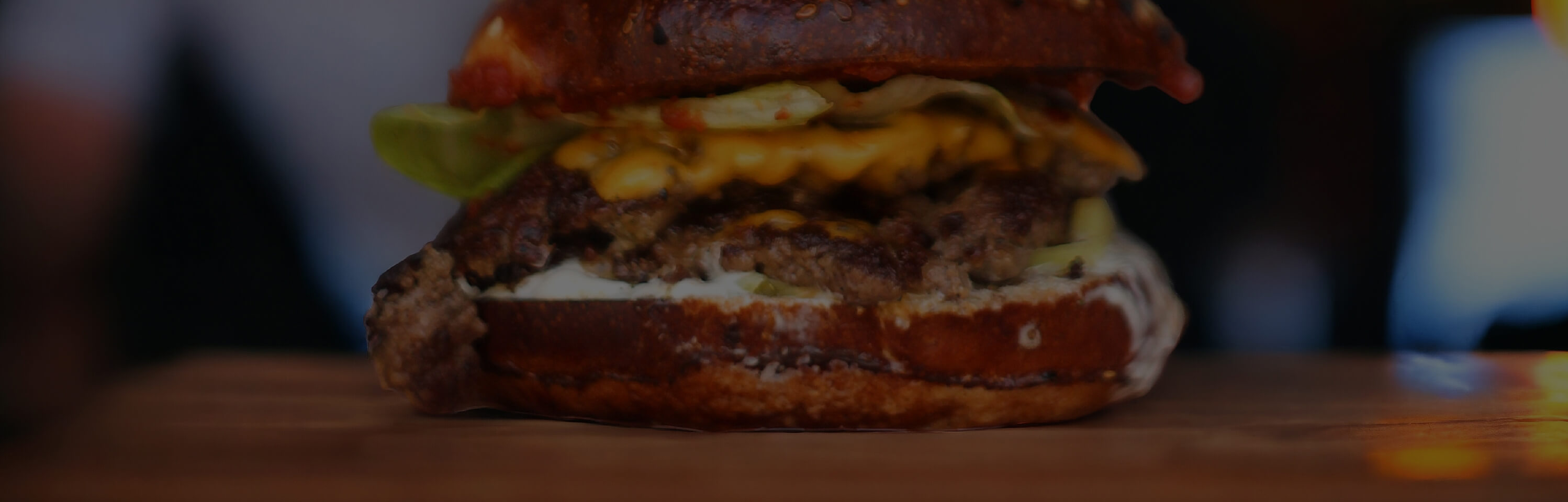 Close-up of a juicy cheeseburger with a thick patty, melted cheese, lettuce, and sauce, all encased in a toasted bun. The burger sits on a wooden surface, showcasing its layers and texture.